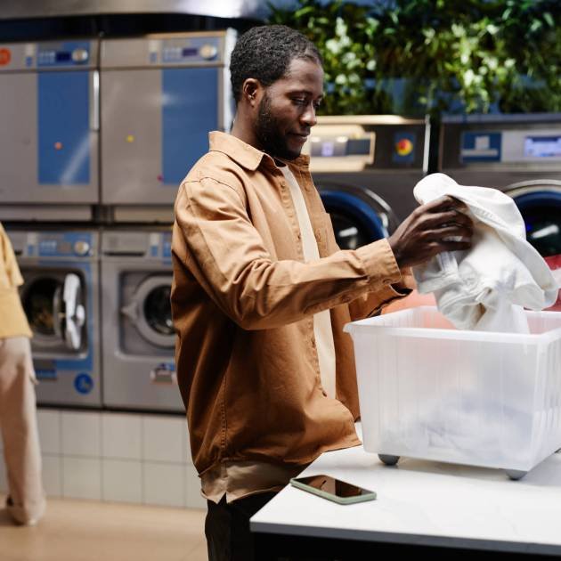 African American man in casualwear preparing dirty clothes for machine wash while standing by table and putting them into container