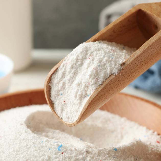 Wooden bowl and scoop with laundry powder, close up